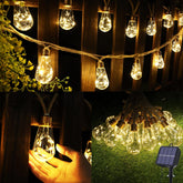 String of illuminated light bulbs with a hand holding one, set against a wooden wall and grassy ground.